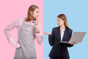Change of traditions. Petite young woman holding a laptop and reprimanding her boyfriend while he...