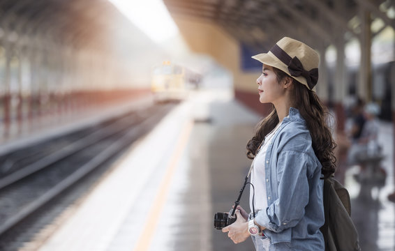 Asian backpack traveler woman with camera standing   at train station platform and waiting train arrivel