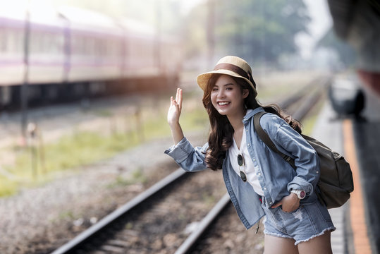 Asian backpack traveler woman smiling and waving hand at train station platform