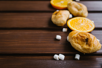 Croissants with oranges and marshmallows on rustic wooden table
