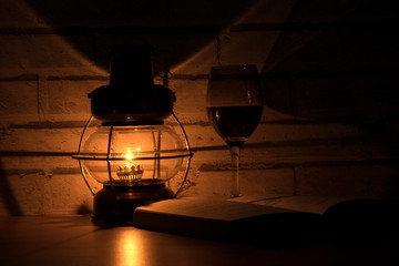 Fototapeta na wymiar Still life.Oil lamp with glass of red wine and open book.