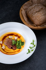 An appetizing pumpkin soup is served in a white plate in a restaurant