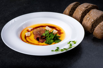 An appetizing pumpkin soup is served in a white plate in a restaurant