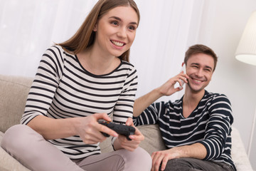 Interesting game. Exuberant smiling woman playing a game and her boyfriend talking on the phone