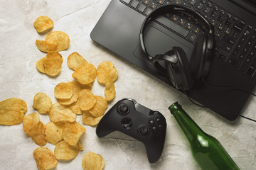 Laptop, Gamepad, Headphones, Potato chips, Bottle of Beer on a light stone background. Concept of...