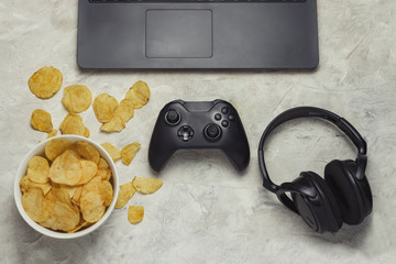 Laptop, Gamepad, Headphones, Potato chips on a light stone background. Concept of computer games...