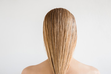 Naklejka premium Wet, blonde, perfect woman's hair after shower on the gray background. Care about beautiful, healthy and clean hair. Beauty salon concept. Young girl's back view.