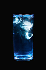 A single-colored transparent cocktail, refreshing shining in a tall blue glass with large square ice cubes. Side view Isolated black background. Drink for the menu restaurant, bar, cafe