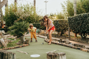 Group of two funny kids playing mini golf, children enjoying summer vacation - obrazy, fototapety, plakaty