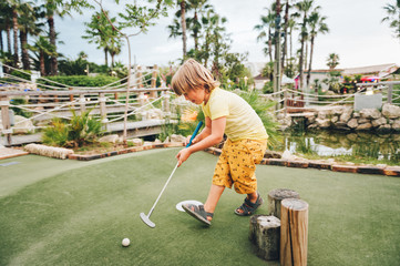 Funny kid boy playing mini golf, child enjoying summer vacation
