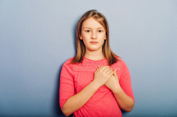 Obraz premium Studio shot of adorable little girl wearing pink dress, posing against purple background, holding hands next to heart