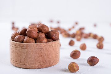 Hazelnuts in brown wooden bowl on white background