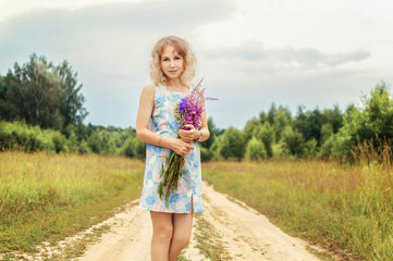 portrait of a beautiful girl in a blue dress holding a bouquet of wildflowers