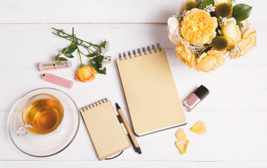 top view of empty open notebook with pen, flowers English rose, cosmetics and cup of tea on table top