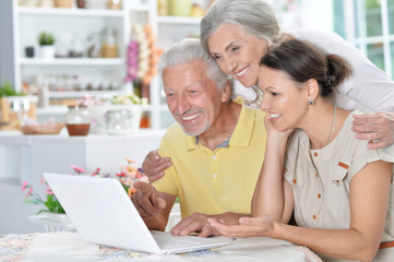 happy senior couple with adult daughter using laptop 