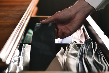 A handsome man with a white shirt, is choosing the tie from the drawer.