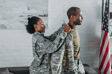 Female soldier helping man to get dressed in camouflage clothes