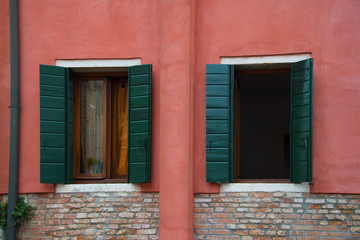 Facade of an old, red Italian building with two windows with green wooden shutters.