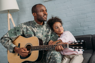 Father in army uniform playing guitar and hugging daughter