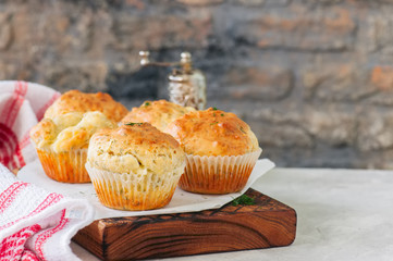 Savory double cheese muffins on a wooden board. White stone background.