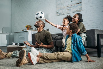Woman and man in army uniform with their children playing with football ball