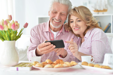 Obraz na płótnie Canvas senior couple with smartphone drinking tea
