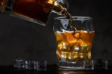 Whiskey bottle flowing into a glass of ice on a dark background