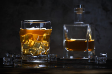 Alcohol in glass with ice and in bottle on dark background
