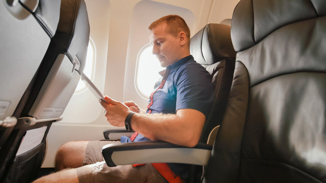 A Young Tourist On The Plane Works With The Tablet Before Leaving.