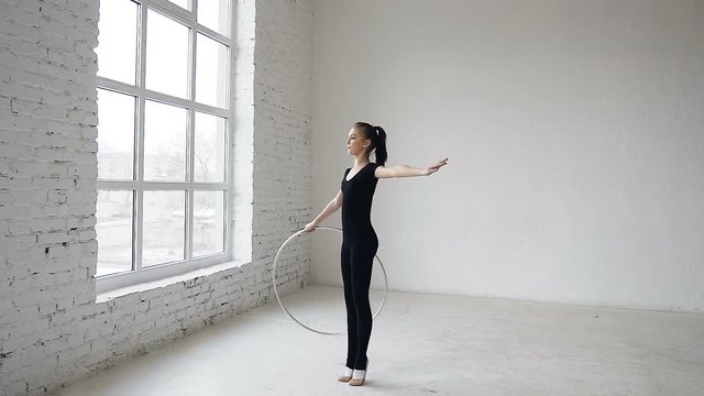 Young attractive girl in black body training a gymnastics exercise with a hoop in the sports school at white background