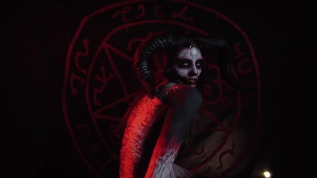 Demoness with big horns bends his back against the background of the pentagram