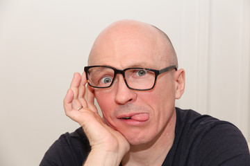 adult bald man in glasses shows tongue
