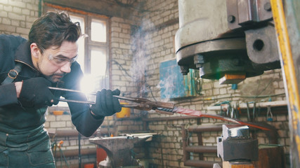 Man blacksmith in workshop forging red hot iron on anvil - small business