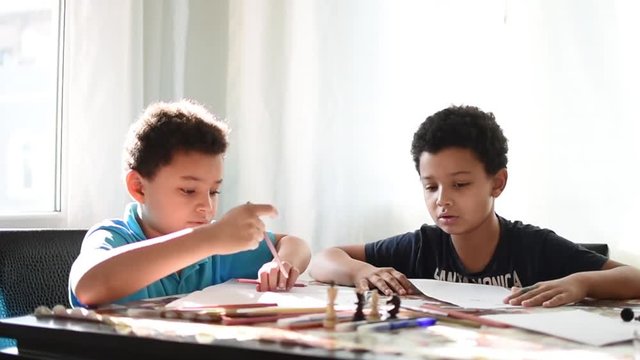 Two brothers sit at the table at home and paint with pencils. Children's hobby. Development of children. The boys do their homework.