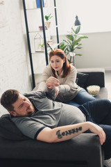 girlfriend taking boyfriends hand and sitting on sofa at home