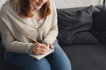 Cropped image of size plus girl writing something to notebook at home