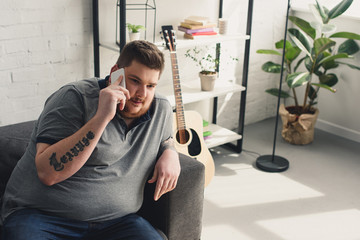 overweight man talking by smartphone on sofa at home - obrazy, fototapety, plakaty