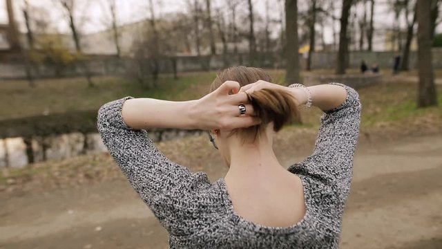 Woman tying her smooth hair in ponytail, making hairdo, back view. Haircare concept.