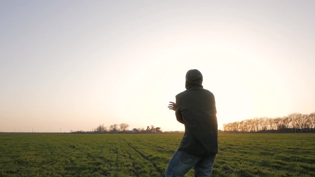 Young man in casual wear practice wushu or karate in spring fields against sunset