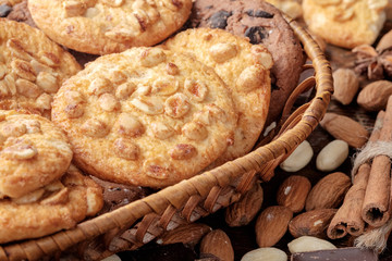 Peanut cookies and chocolate chips cookies in wicker basket and scattered nuts near it. Close-up view.