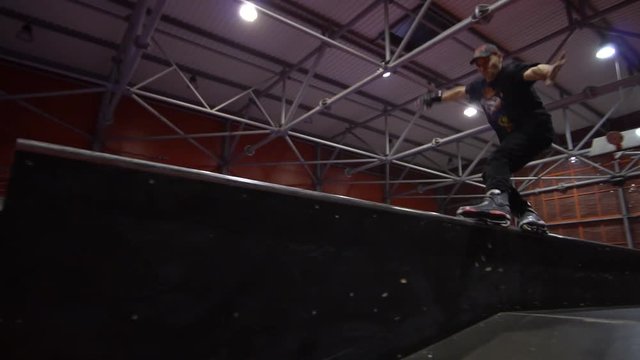 A man in a cap performs a rollerblading trick in an extreme park, slow motion