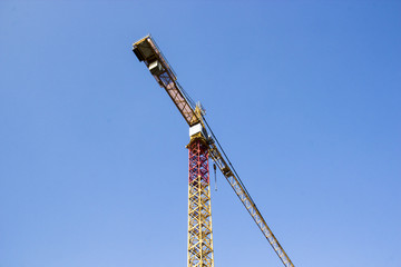 One big yellow construction cranes on blue sky background