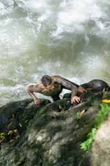 overhead view of tattooed man climbing on rocks with river on background, Bali, Indonesia