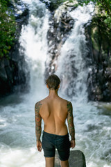 Fototapeta na wymiar back view of tattooed man standing with Aling-Aling Waterfall on background, Bali, Indonesia