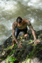 overhead view of tattooed man climbing on rocks with river on background, Bali, Indonesia