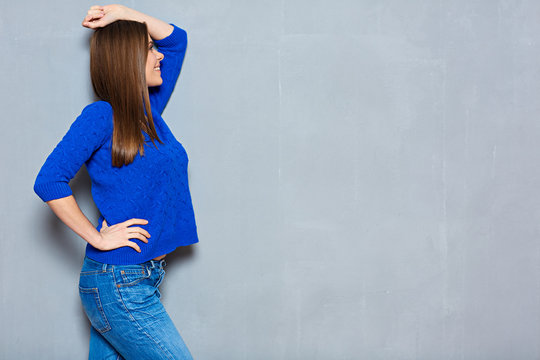 Happy woman wearing blue sweater and jeans with hand raised up.