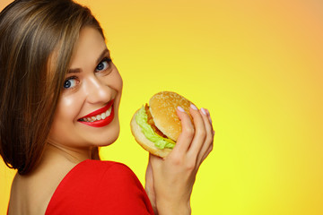 Smiling girl holding burger looks over shoulder.