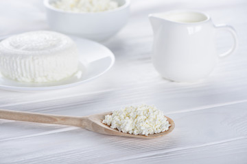 close-up view of fresh healthy cottage cheese in wooden spoon and dairy products on table