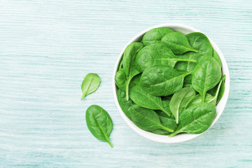 Fototapeta premium Green spinach leaves in bowl on table top view. Healthy food.