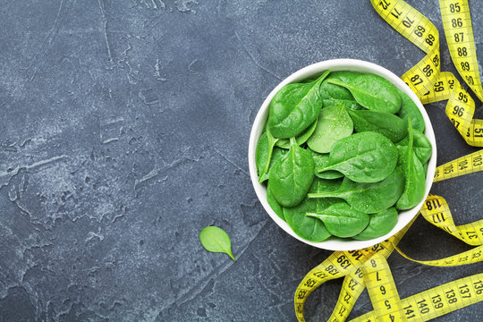 Yellow tape measure and green spinach leaves from above. Diet food concept.
